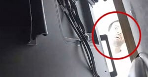 A close-up, low-angle view shows a person's face peering into a gap between a dark, metallic object with cables and a wooden surface, highlighted by a red circle.