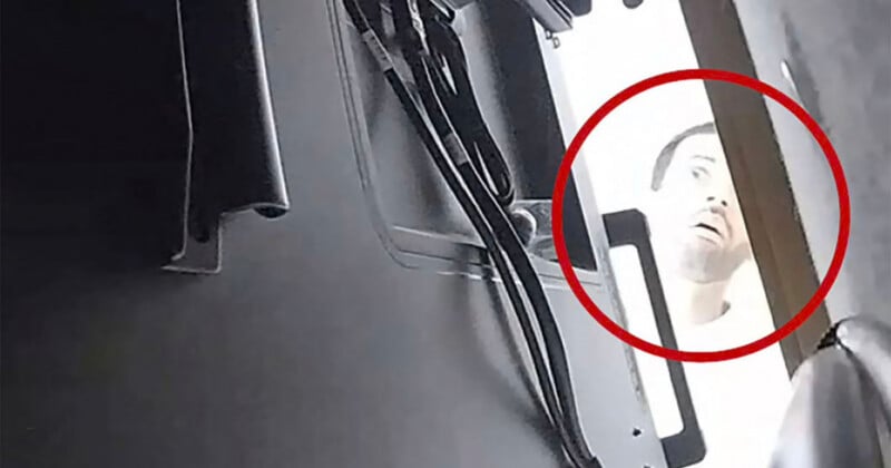 A close-up, low-angle view shows a person's face peering into a gap between a dark, metallic object with cables and a wooden surface, highlighted by a red circle.