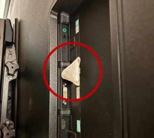 A piece of crumpled white paper is wedged into the side input panel of a television, highlighted by a red circle.