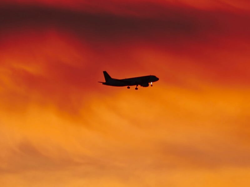 A silhouette of an airplane in flight against a vibrant orange and red sunset sky.