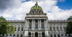 The Pennsylvania State Capitol building features a large green dome topped with a golden statue under a cloudy sky.