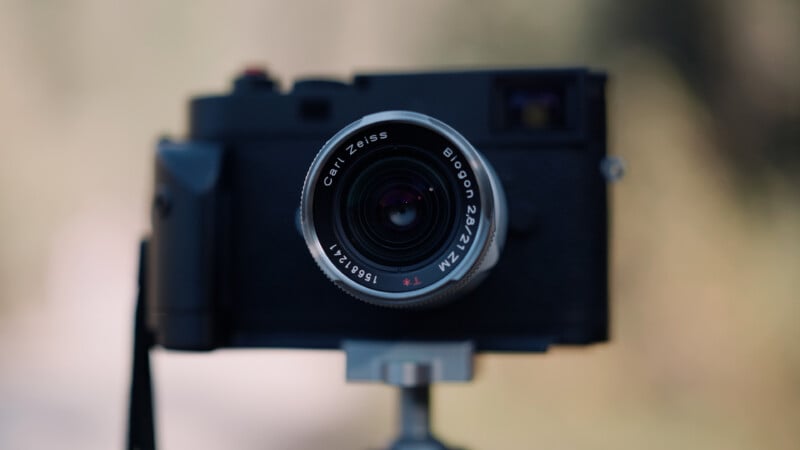 A black camera with a silver Carl Zeiss Biogon 2.8/21 ZM lens mounted on a tripod against a blurred background.