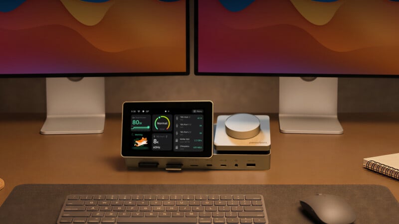 A desk setup featuring a dual-monitor display, a keyboard, a mouse, and a central docking station with a digital screen showing device status.