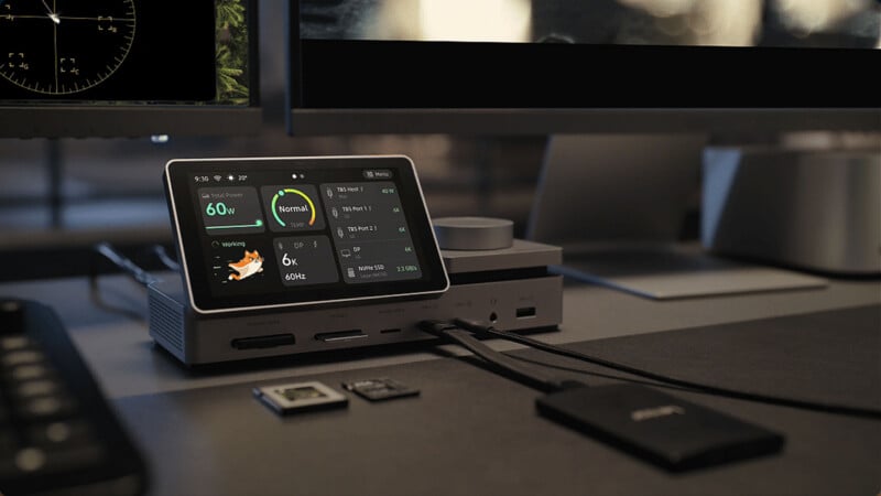 A desktop docking station with a built-in touchscreen display showing system status, connected to various cables and memory cards on a desk.