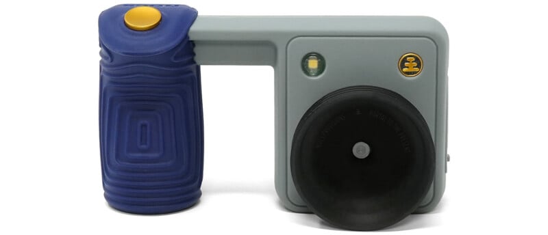 A gray and blue handheld device with a gold button, a small LED light, and a large black circular lens housing.