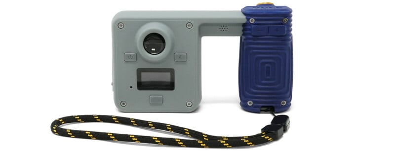 A gray and blue digital camera with a wrist strap, featuring a lens, a small screen, and control buttons on its front face.