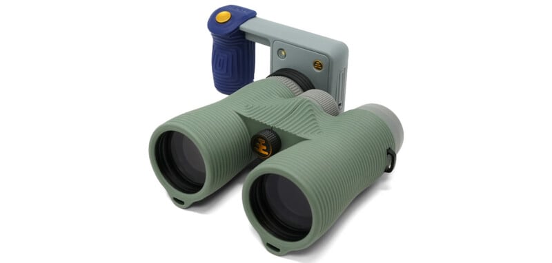 Sage green binoculars with a textured, ribbed grip and a detachable blue and grey handle attachment featuring a yellow button.