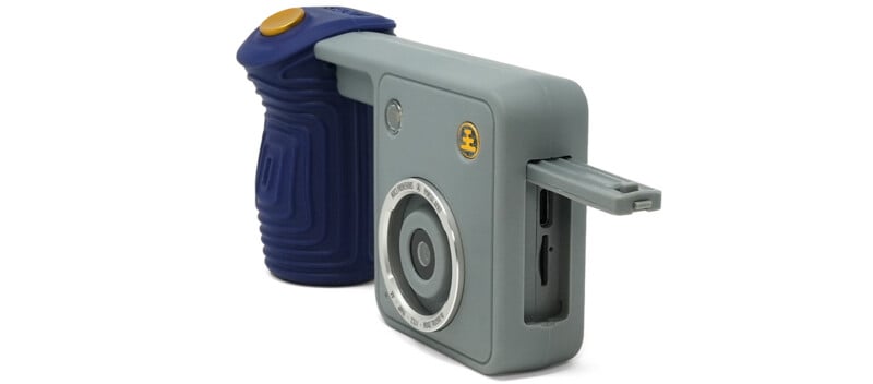A gray digital camera with a blue rubberized grip and a gold shutter button, shown with its side port cover open to reveal a USB-C port and memory card slot.