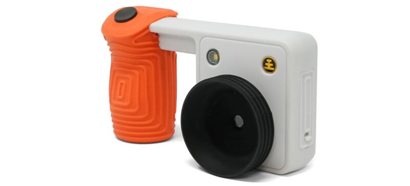 A white, rectangular monocular device with a black rubber eyecup and an attached orange, textured grip handle with a black button on top.