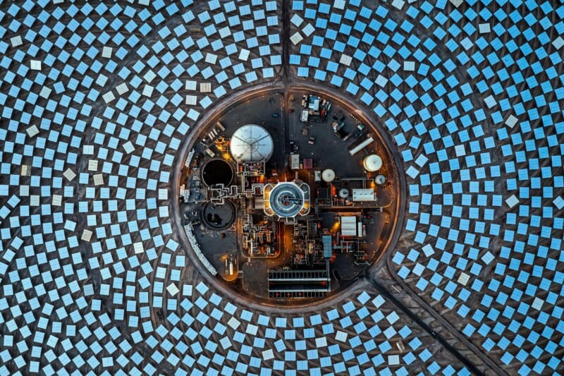 An aerial view of a concentrated solar power plant with a central tower surrounded by a dense, circular array of reflective mirrors.