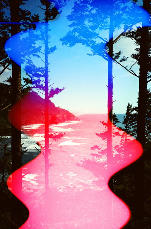 A coastal landscape viewed through trees is overlaid with a vertical, wavy band of bright blue and pink light leaks.