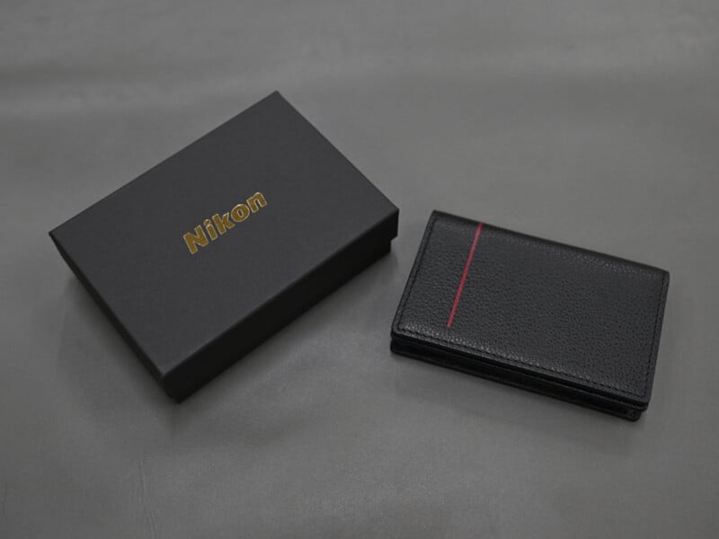 A black Nikon-branded gift box sits next to a black leather card holder with a single vertical red stripe.