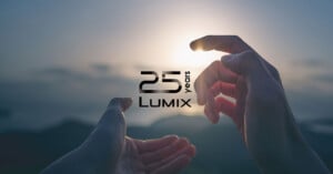Two hands reach toward a setting sun against a blurred mountain landscape, with the text "25 years LUMIX" centered in the middle.