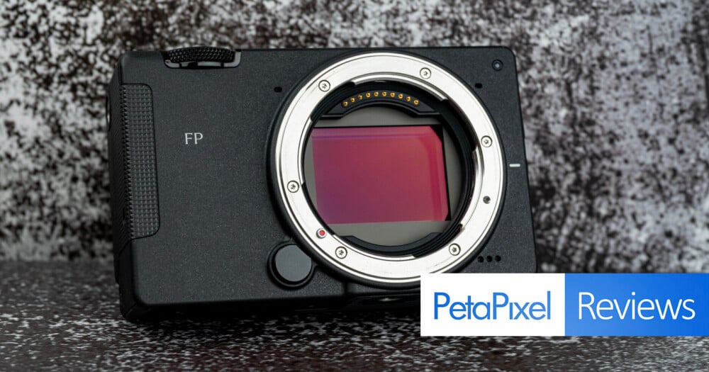 A black digital camera body with a prominent lens mount and sensor is positioned against a textured gray background, with a PetaPixel Reviews logo in the bottom right corner.