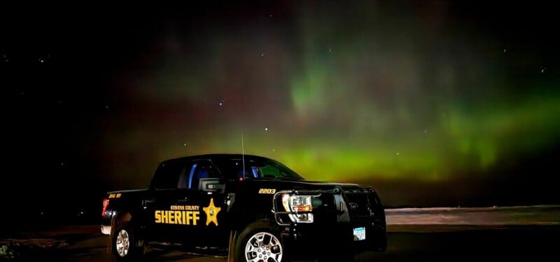 A black Stevens County Sheriff pickup truck is parked at night under a vibrant green aurora borealis.