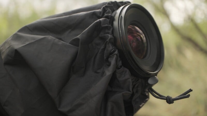 A camera lens covered by a black protective rain sleeve, with a drawstring tightened around the front element.