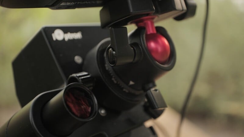 A close-up view of an iOptron telescope mount featuring a red ball head and a polar alignment scope.