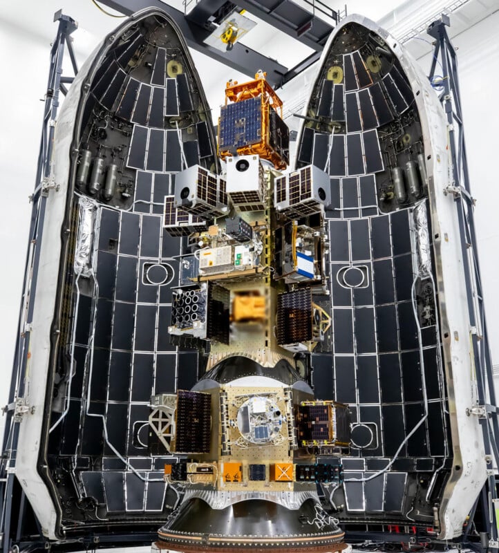 A large rocket payload fairing is open, revealing a central stack of multiple small satellites mounted on a launch vehicle adapter.