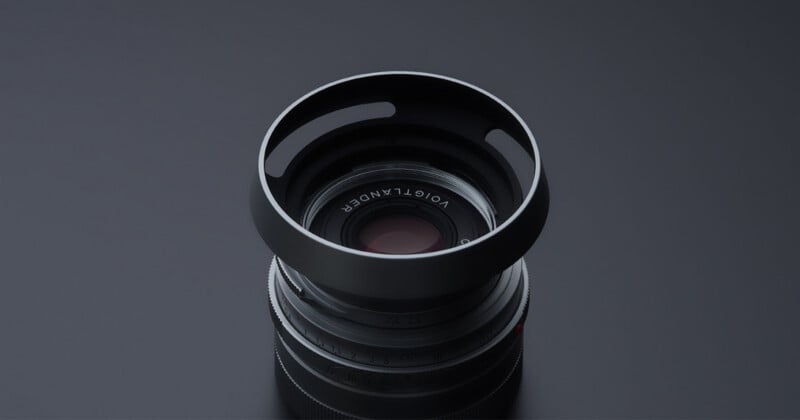 A Voigtländer camera lens with a vented metal hood, viewed from directly above against a dark gray background.