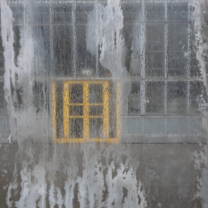 A bright yellow window frame is visible through a pane of glass covered in streaks of water and condensation.