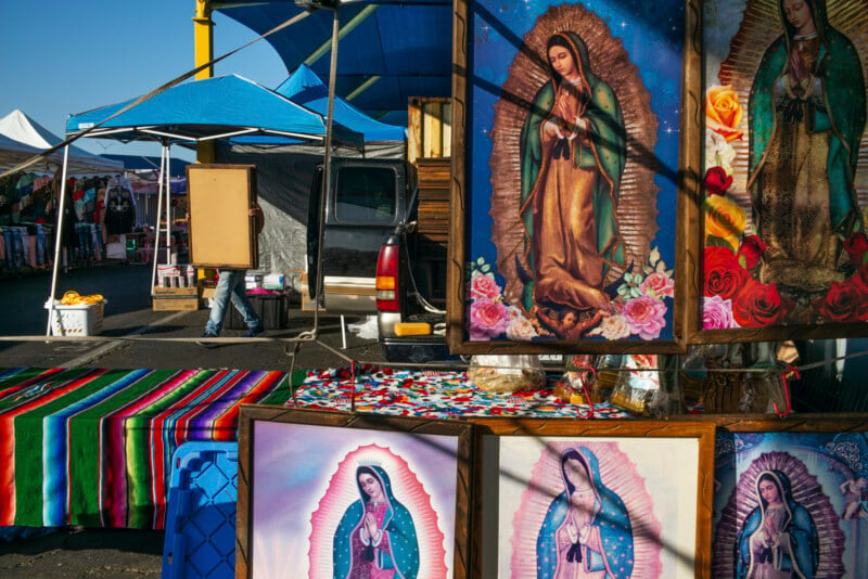 A vendor carries a framed picture past a market stall displaying several framed images of the Virgin of Guadalupe.