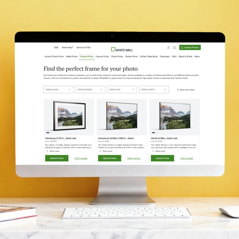 A computer monitor displays the WhiteWall website, showcasing a selection of framed photo prints with filtering options and product details.