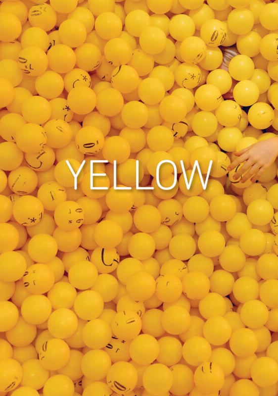 A hand reaches into a large pit filled with yellow plastic balls, many of which are printed with simple black facial expressions.