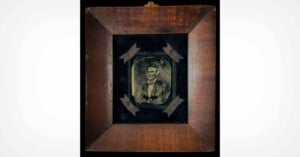 A framed daguerreotype portrait of Abraham Lincoln centered on a black velvet background with four ribbon accents in a wooden frame.