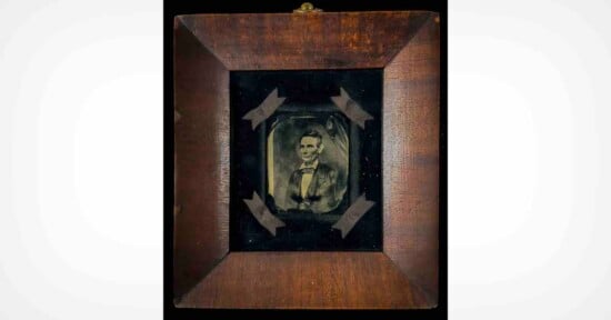 A framed daguerreotype portrait of Abraham Lincoln centered on a black velvet background with four ribbon accents in a wooden frame.