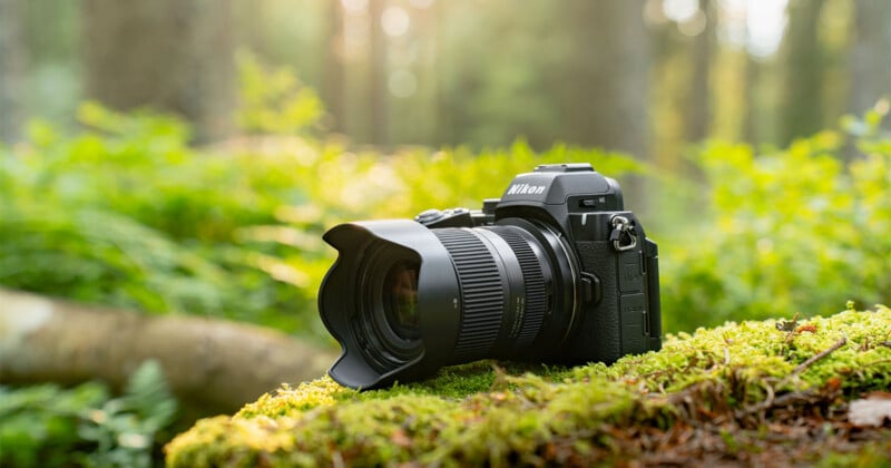 A black Nikon mirrorless camera with a lens attached rests on a moss-covered log in a sunlit forest.