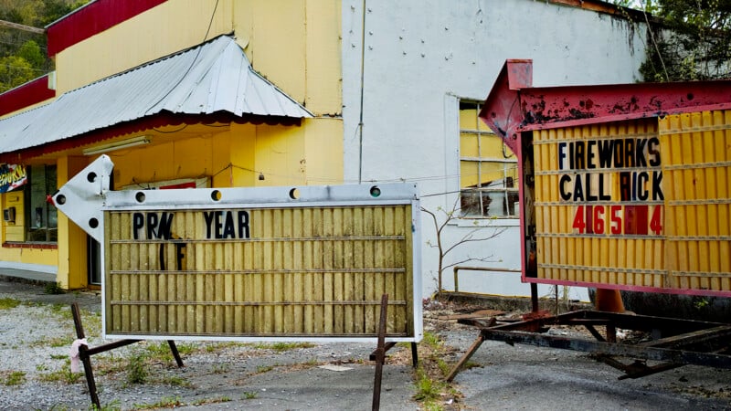 Two weathered, portable signs stand in front of a dilapidated building with yellow and white walls.