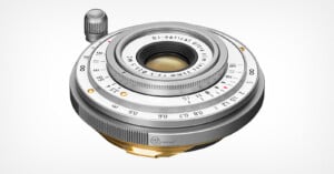 A silver, ultra-slim 35mm f/3.5 manual focus camera lens with a gold-colored mount, viewed from a high angle against a white background.