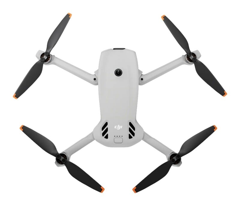 A top-down view of a light gray quadcopter drone with four black propellers featuring orange tips, positioned against a white background.