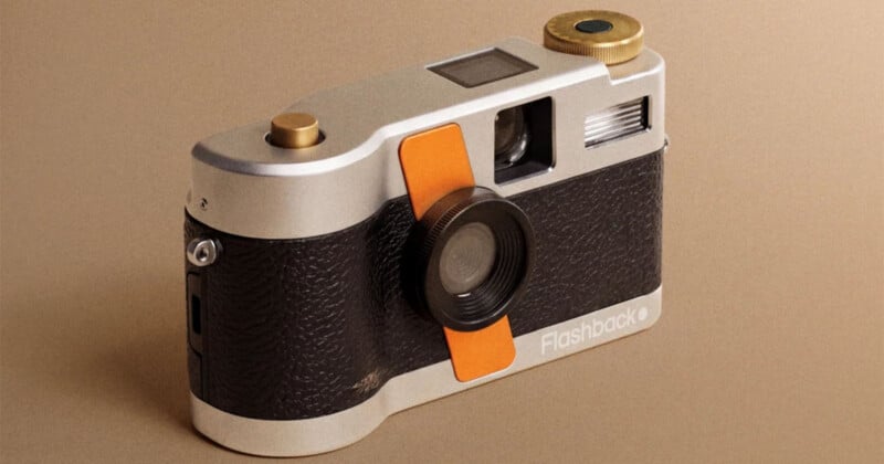 A silver and black digital camera with an orange accent strip and brass-colored top dials, featuring the word "Flashback" on the front.