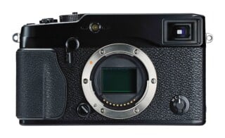 A front view of a black mirrorless digital camera body with an exposed sensor and a focus mode selector dial labeled M, C, and S.