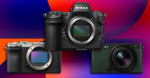 Three digital cameras are arranged against a colorful, abstract background: a silver Sony E-mount camera on the bottom left, a black Nikon Z-series camera in the center, and a dark green Panasonic Lumix camera on the bottom right.