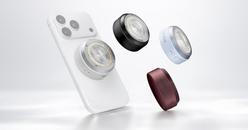 A white smartphone with a circular magnetic light attached to its back, surrounded by three additional lights in black, light blue, and dark red.