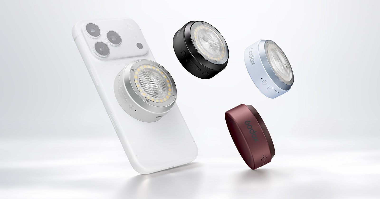 A white smartphone with a circular magnetic light attached to its back, surrounded by three additional lights in black, light blue, and dark red.
