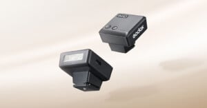 Two black Godox iM10 compact flashes are shown against a light beige background, one displaying its front light panel and side USB-C port, and the other showing its top control buttons and battery indicator lights.
