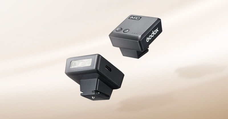 Two black Godox iM10 compact flashes are shown against a light beige background, one displaying its front light panel and side USB-C port, and the other showing its top control buttons and battery indicator lights.