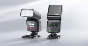 Two Godox TT350II camera flashes stand on a light gray surface, one angled to the side and the other facing forward with its digital display illuminated.