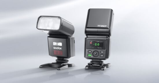 Two Godox TT350II camera flashes stand on a light gray surface, one angled to the side and the other facing forward with its digital display illuminated.