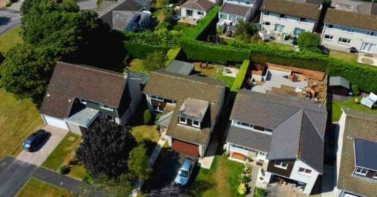An aerial view shows three suburban houses with driveways, lawns, and a backyard under construction with wooden fencing.