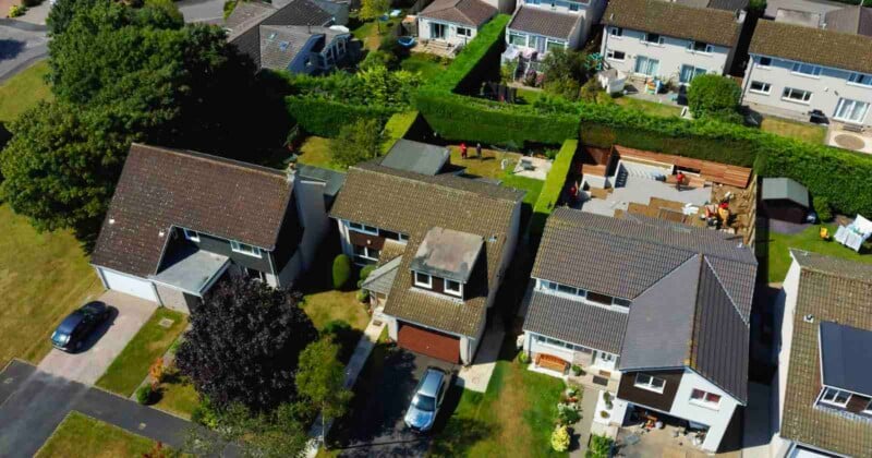 An aerial view shows three suburban houses with driveways, lawns, and a backyard under construction with wooden fencing.
