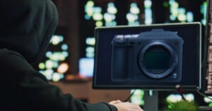 A person in a dark hoodie sits at a computer, with a digital overlay of a Hasselblad camera body displayed on the screen.