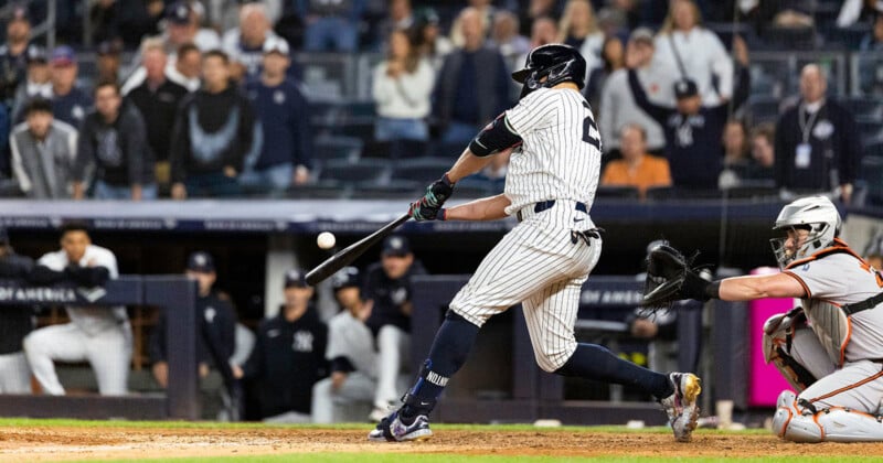 A baseball player in a pinstriped uniform swings a bat at a ball, with a catcher crouching behind home plate.