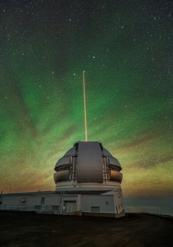A large observatory dome sits under a starry night sky with a green airglow, emitting a bright orange laser beam upward.