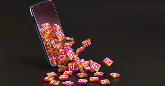 A smartphone sits at an angle on a dark surface, with numerous 3D Instagram Reels icons spilling out from its screen.