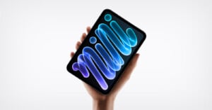 A hand holds a small tablet with a dark screen displaying an abstract blue, glowing, ribbon-like graphic against a white background.