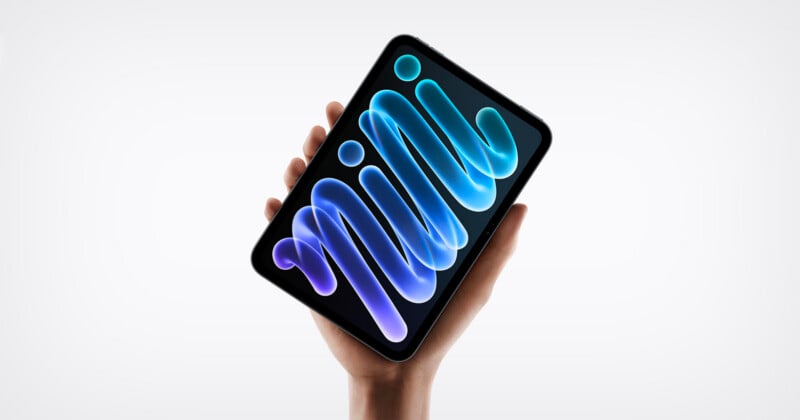 A hand holds a small tablet with a dark screen displaying an abstract blue, glowing, ribbon-like graphic against a white background.